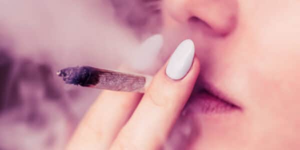 Close-up photograph of a woman smoking a marijuana cigarette.