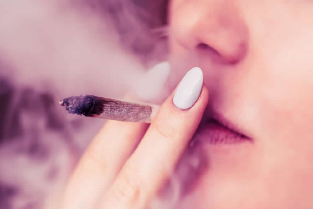 Close-up photograph of a woman smoking a marijuana cigarette.
