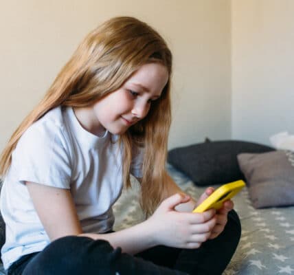 Photo of a young girl fully absorbed in her bright yellow phone.