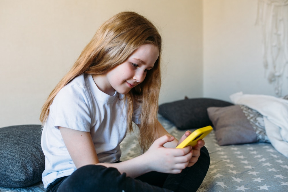 Photo of a young girl fully absorbed in her bright yellow phone.