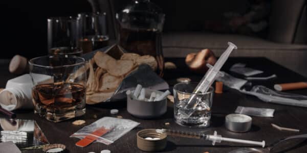 Photo of a table covered with multiple substances of abuse, including cigarettes, alcohol, powders, pills, and junk food.