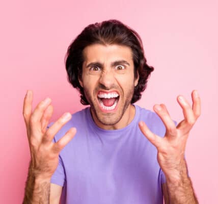 Photo of a stressed-out man in a purple shirt on a pink background.