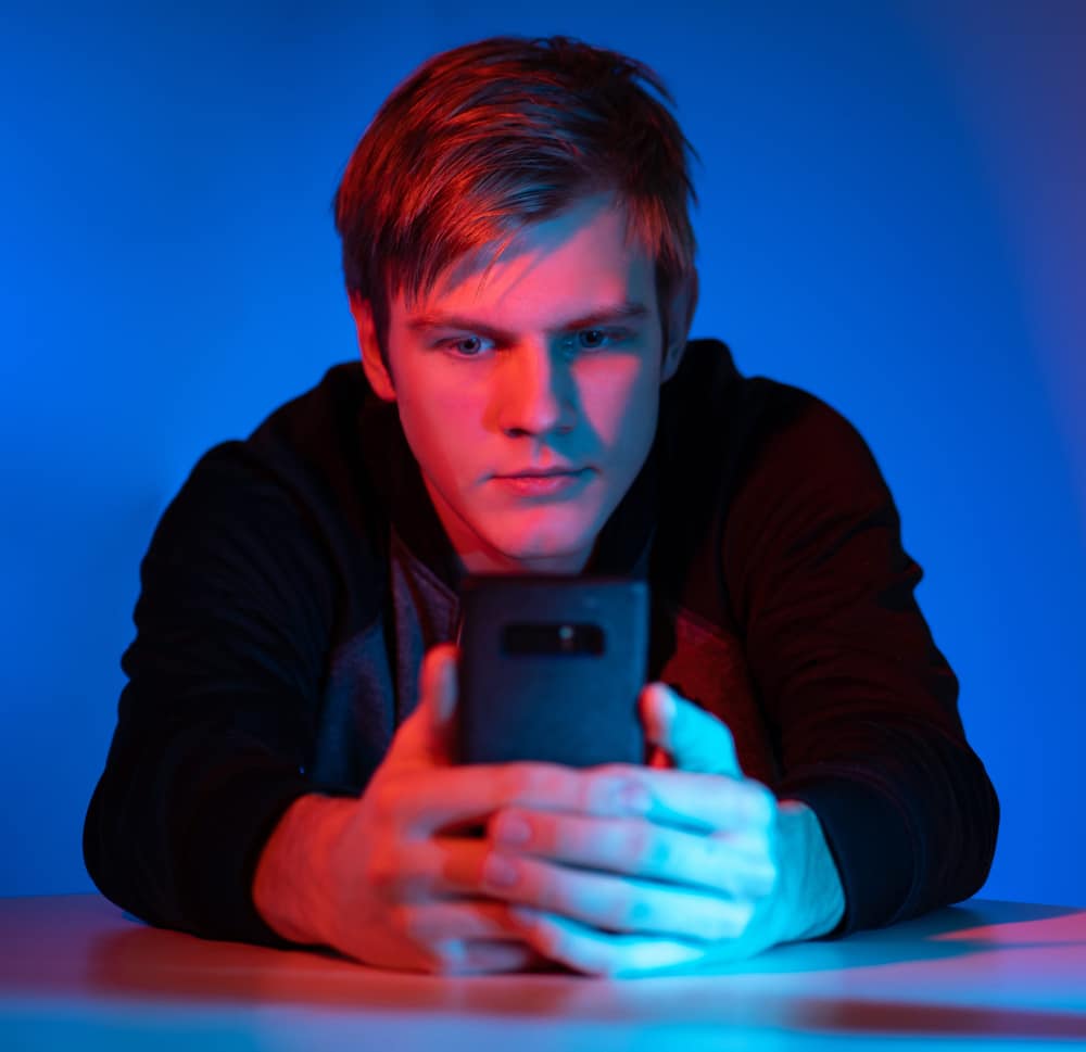 Photograph of a young man seated at a table mesmerized by his smartphone.