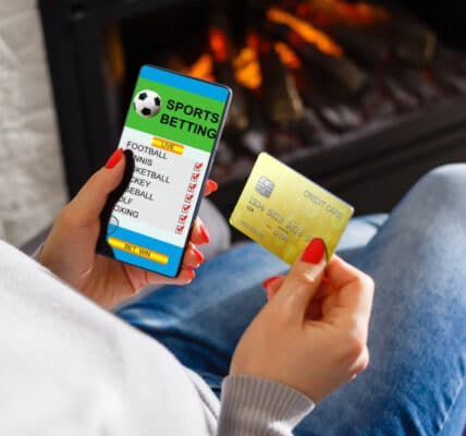 Photo of a woman placing sports bets through her phone using a credit card.