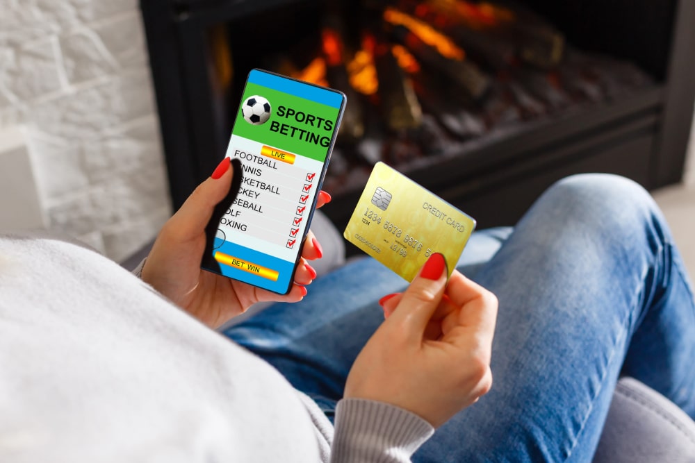 Photo of a woman placing sports bets through her phone using a credit card.