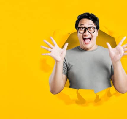 Asian man in eyeglasses with excited expression with torn paper background indicating a breakthrough.