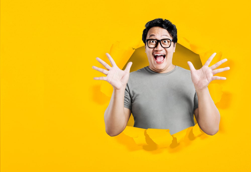 Asian man in eyeglasses with excited expression with torn paper background indicating a breakthrough.