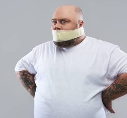 Photo of an overweight man in a white T-shirt with masking tape around his mouth as a metaphor for muting stress-related eating.