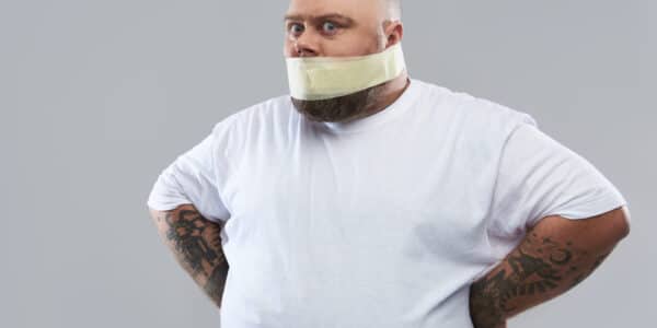 Photo of an overweight man in a white T-shirt with masking tape around his mouth as a metaphor for muting stress-related eating.