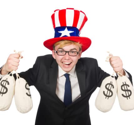 Photo of a boy in a suit and tie with an Uncle Sam top hat holding two money bags in each hand and laughing.