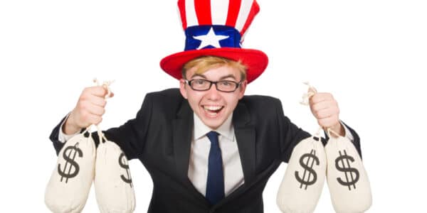 Photo of a boy in a suit and tie with an Uncle Sam top hat holding two money bags in each hand and laughing.