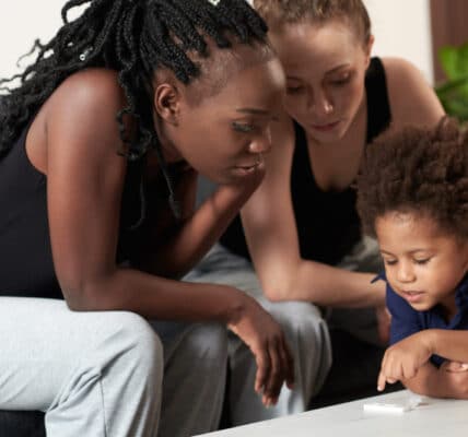A young therapist looks on as a mother and child interact during an in-home therapy session.