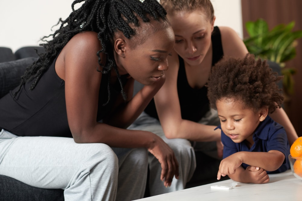 A young therapist looks on as a mother and child interact during an in-home therapy session.