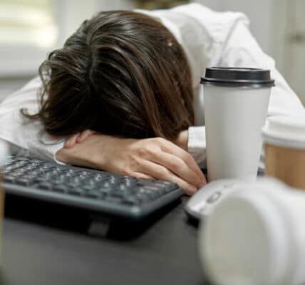 Photo of office worker asleep at her desk surrounded by coffee cups.