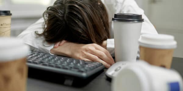 Photo of office worker asleep at her desk surrounded by coffee cups.