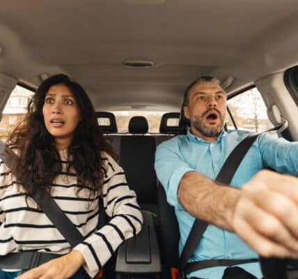 Photo of a man and a woman in the front seat of a car with panicked looks on their faces.