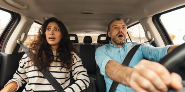 Photo of a man and a woman in the front seat of a car with panicked looks on their faces.