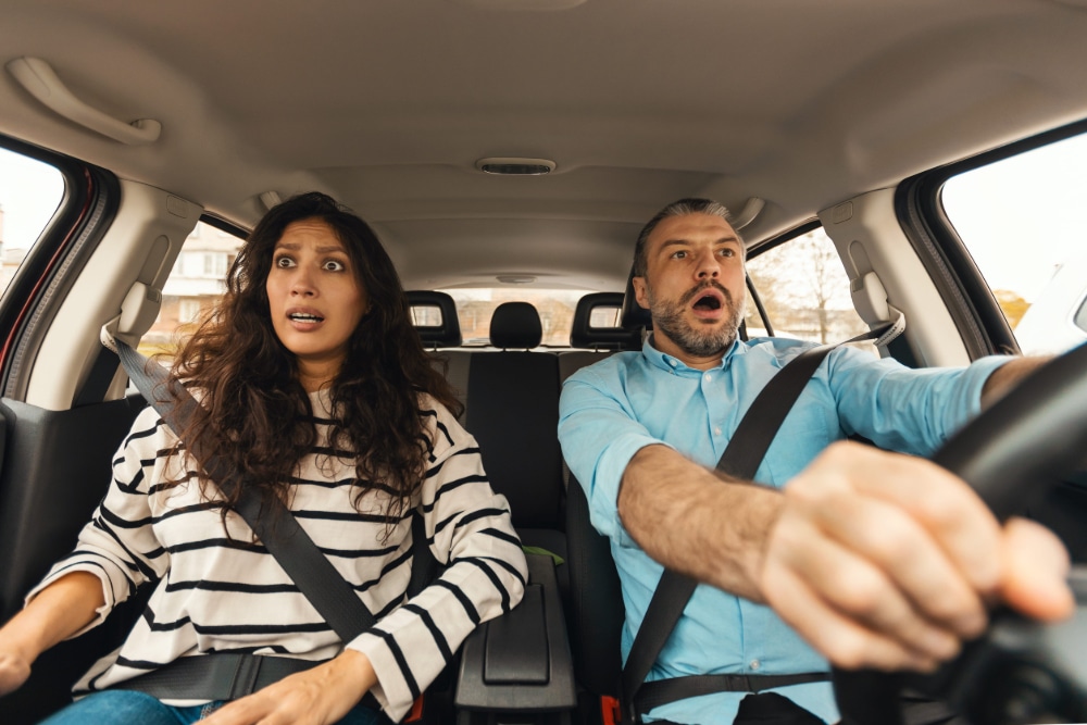 Photo of a man and a woman in the front seat of a car with panicked looks on their faces.