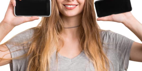 Photo of a young woman holding up two smartphones.