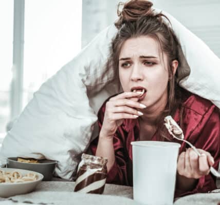 Photo of a depressed woman in bed eating ice cream and other treats.