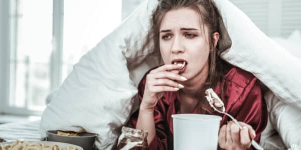 Photo of a depressed woman in bed eating ice cream and other treats.
