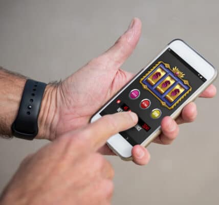 Photo of a mans hands holding a smartphone and playing a slot machine style gambling game.