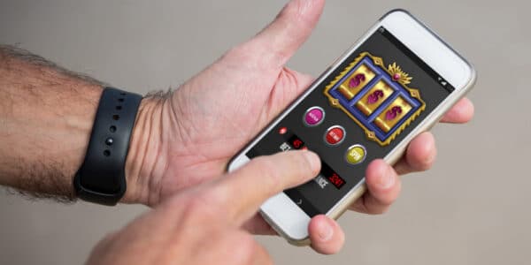 Photo of a mans hands holding a smartphone and playing a slot machine style gambling game.