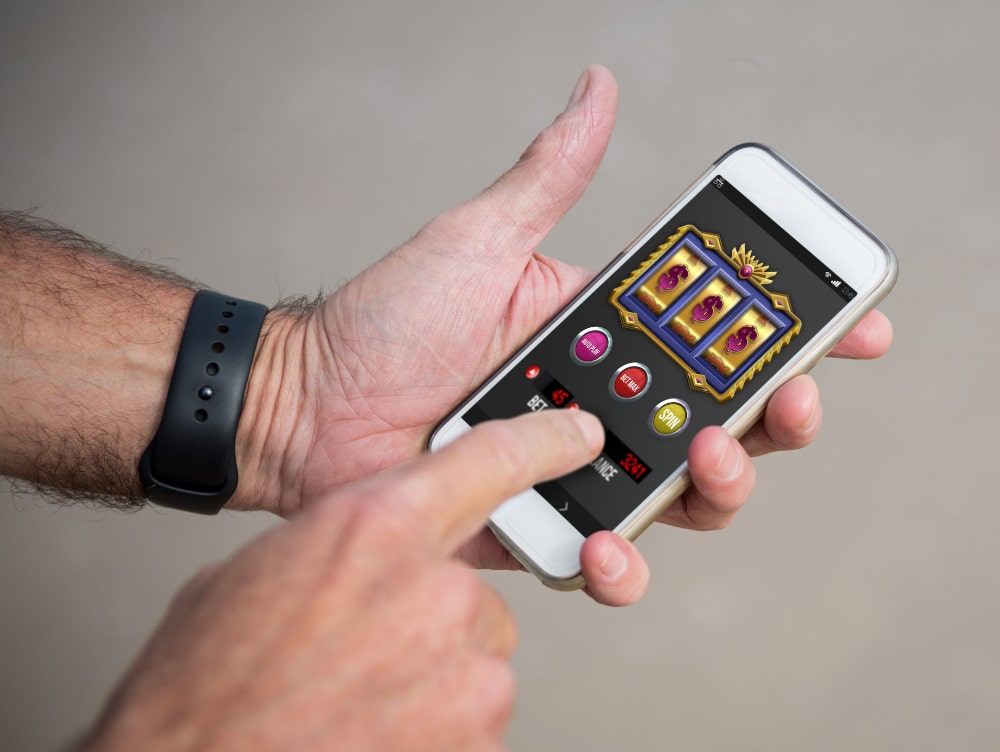 Photo of a mans hands holding a smartphone and playing a slot machine style gambling game.