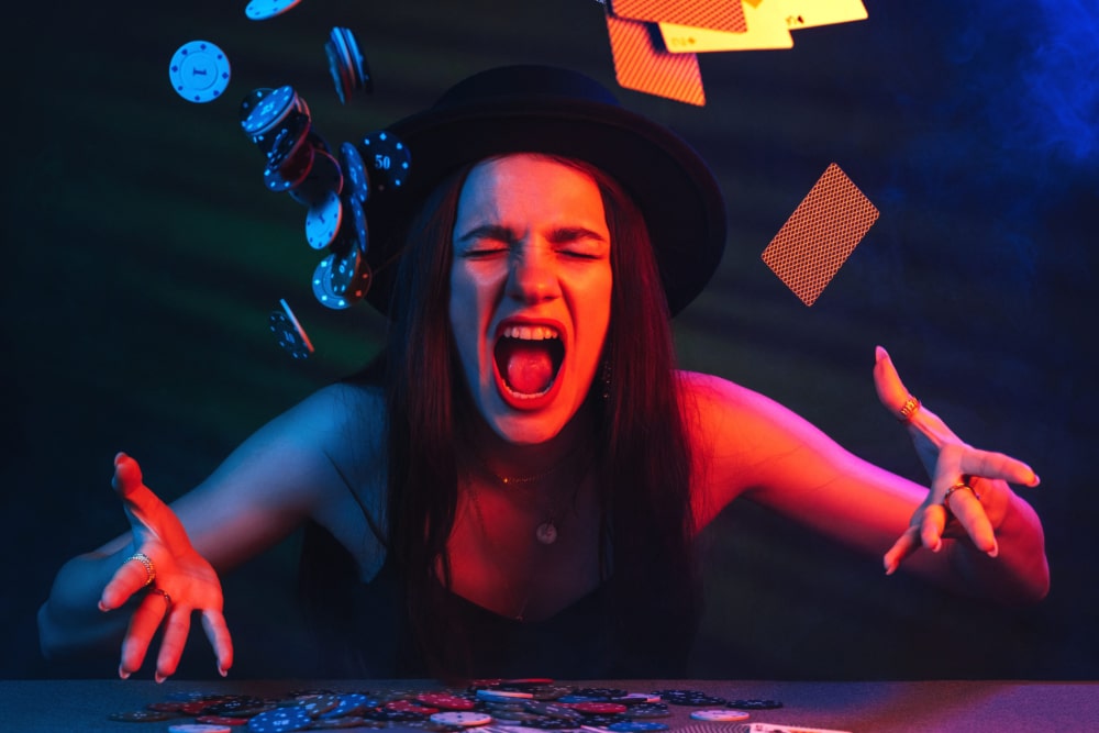 Photo of angry woman throwing poker chips and playing cards into the air in what looks like a dimly lit casino.