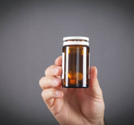 Photo of a man's hand holding a partially used container of pain pills.