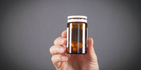Photo of a man's hand holding a partially used container of pain pills.