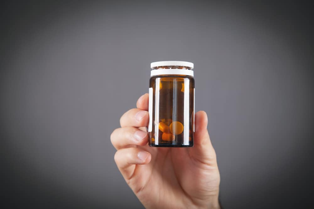 Photo of a man's hand holding a partially used container of pain pills.