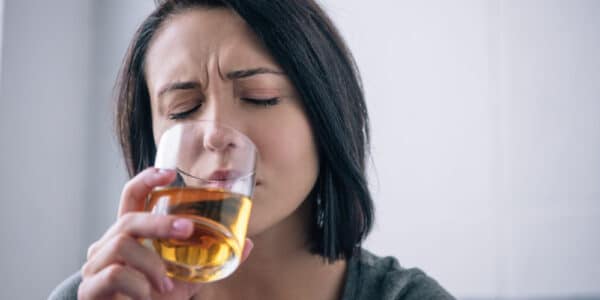 Photography of a woman with a distressed expressions drinking what looks like bourbon from a glass.