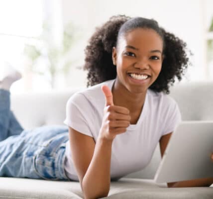 Teenaged girl holding a tablet computer and smiling with a big thumbs up.