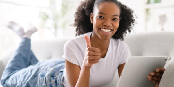 Teenaged girl holding a tablet computer and smiling with a big thumbs up.
