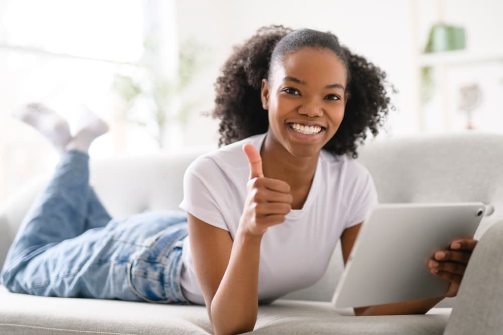 Teenaged girl holding a tablet computer and smiling with a big thumbs up.