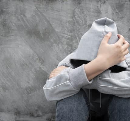 Photo of a youth with a hoody sweatshirt pulled up over his or her head with arms crossed covering his or her face.