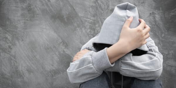 Photo of a youth with a hoody sweatshirt pulled up over his or her head with arms crossed covering his or her face.