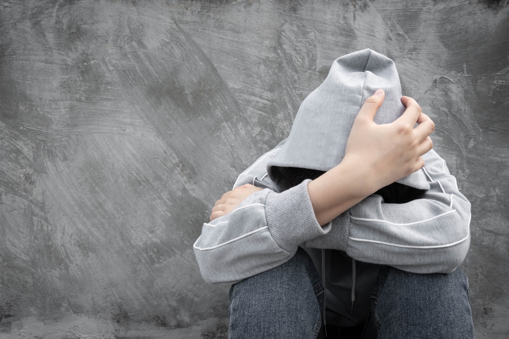 Photo of a youth with a hoody sweatshirt pulled up over his or her head with arms crossed covering his or her face.