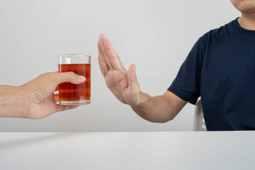Photo of a man refusing a drink by holding up his hand against it.