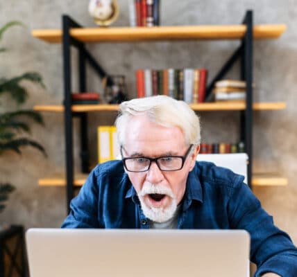 Photo of a senior man who is gambling using his laptop computer and looking shocked at the results.
