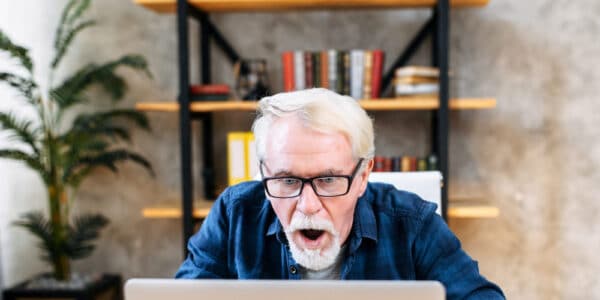 Photo of a senior man who is gambling using his laptop computer and looking shocked at the results.