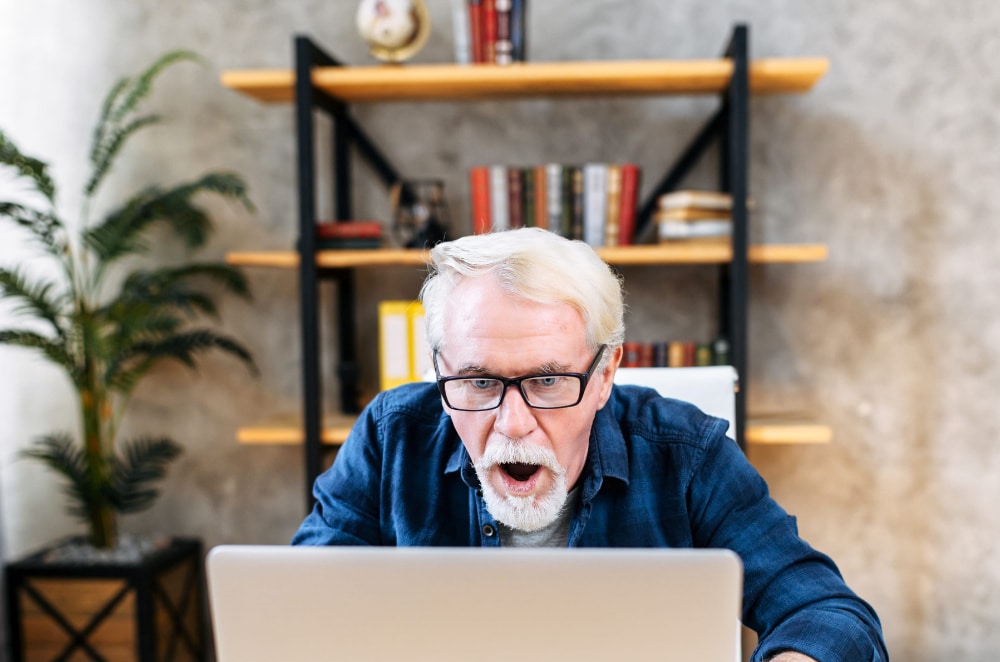 Photo of a senior man who is gambling using his laptop computer and looking shocked at the results.