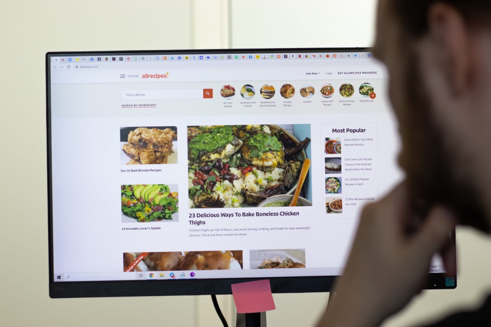 Photo of a man looking at a computer screen filled with images of delicious foods.