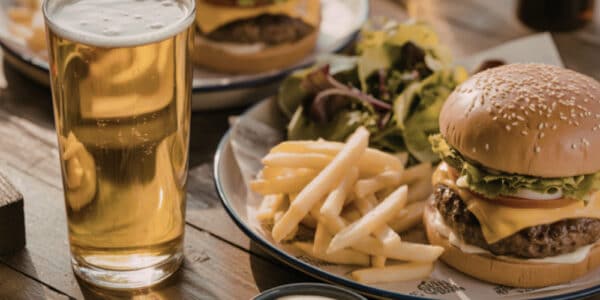 Photo of plates piled high with cheeseburgers and fries plus a pint of amber beer.