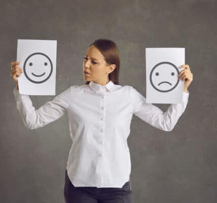 Photo of a woman holding up a happy face sign in one hand and a sad face sign in the other.
