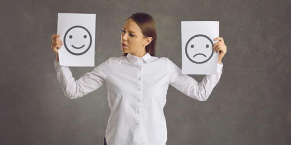 Photo of a woman holding up a happy face sign in one hand and a sad face sign in the other.