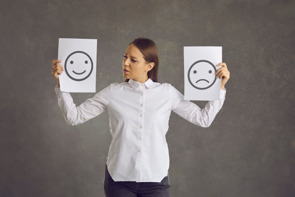 Photo of a woman holding up a happy face sign in one hand and a sad face sign in the other.