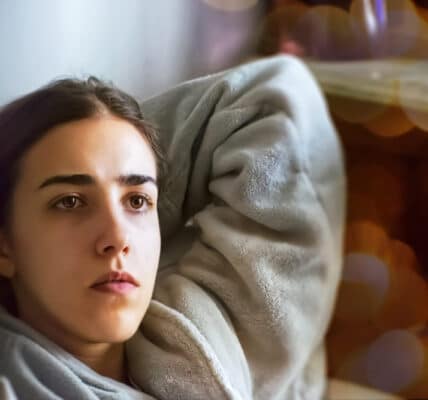 Photograph of a young woman laying in bed unable to sleep due to stressful thoughts.