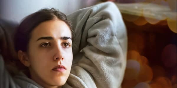Photograph of a young woman laying in bed unable to sleep due to stressful thoughts.